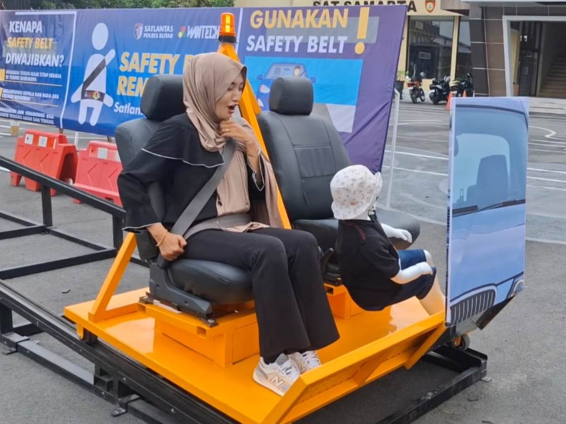 Pemohon SIM di Satlantas Polres Blitar mencoba alat peraga sabuk keselamatan, untuk mengingatkan pentingnya tertib lalu lintas, agar tidak terjadi efek fatal saat berkendara seperti boneka yang terlempar disebelahnya (Novianto, tagarjatim.id)